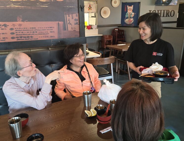 A woman in a black shirt smiles and chats to a table of people in a restaurant.