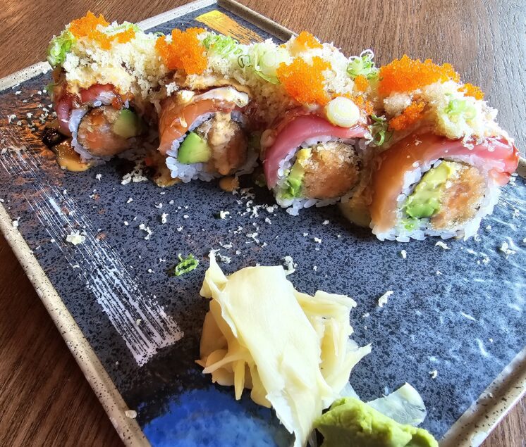 a specialty roll rests on a plate with ginger and wasabi